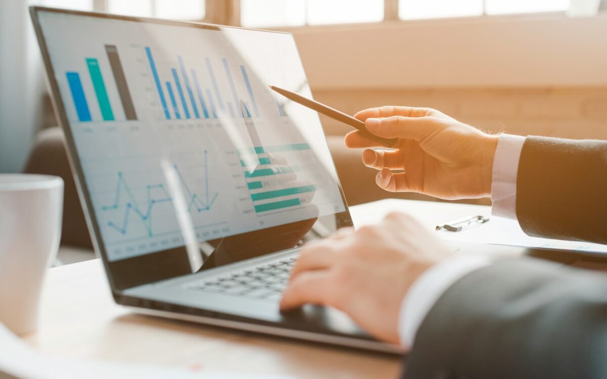 Businessman pointing a pen at bar and line charts on a laptop screen, with a coffee cup on the desk beside him