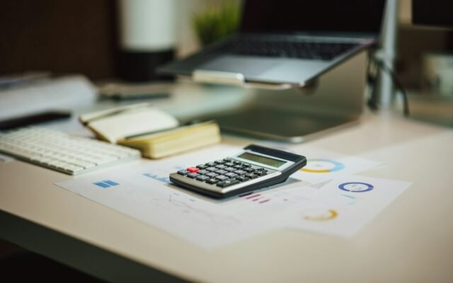 Calculator and financial charts on a desk next to a laptop