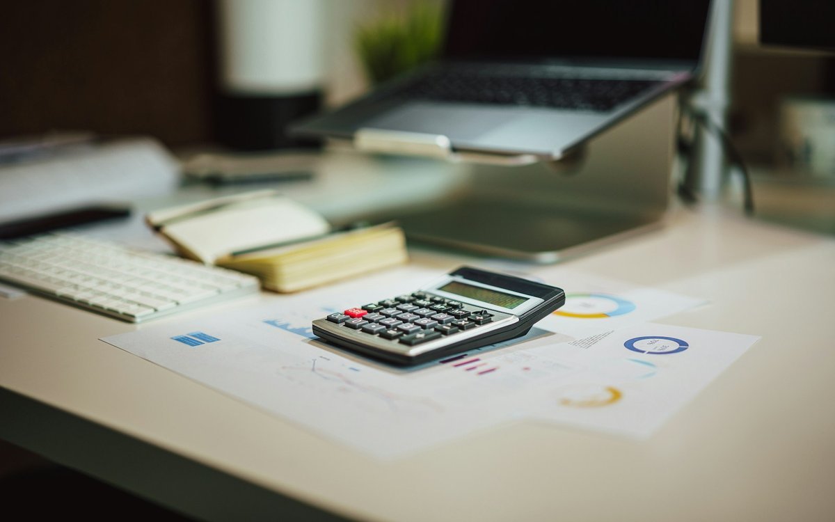 Calculator and financial charts on a desk next to a laptop