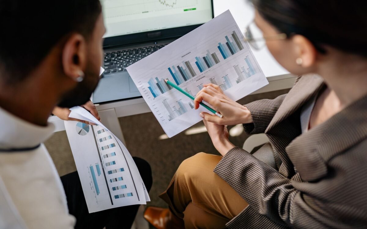 Two colleagues going through printed bar charts together at a desk, with a laptop open behind them