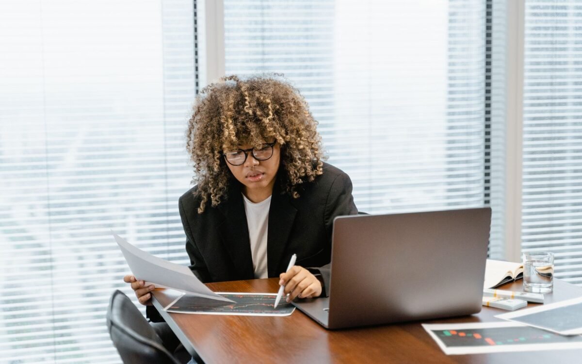 a woman writing on a paper while in front of a laptop